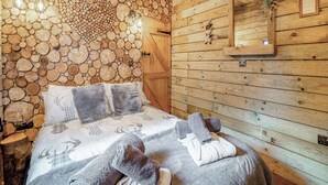 A wooden cabin interior with a bed, a wall of stacked logs, a wooden door, and a mirror. - The Retreat - UK50421 (Ringwood, New Forest)