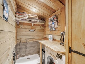 Una habitación pequeña de madera con lavadora, un perchero y ducha.