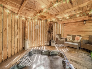 Interior de una cabaña de madera con jacuzzi, muebles de mimbre e iluminación de luces colgantes.