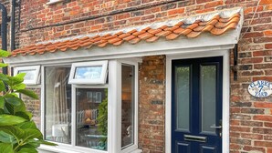 A brick building with a white window and a dark blue door, a sign reading "Clarks Yard", and a small white structure with a window.