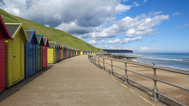A seaside promenade with colorful beach huts and a metal railing along the beach.