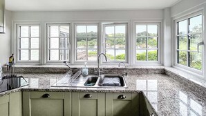 Una cocina con encimera de granito, pileta doble y vista a un jardín a través de amplios ventanales.