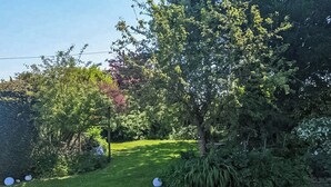 A well-maintained garden with a variety of trees and shrubs, a grassy lawn, and a wooden fence.