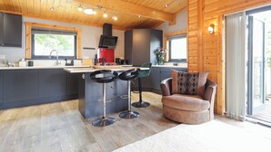 A modern kitchen with a central island, bar stools, a sofa, and a sliding glass door leading to an outdoor area.