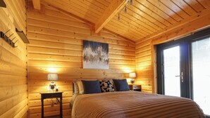 A log cabin bedroom with a bed, two bedside tables with lamps, a rug, and a painting on the wall.