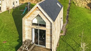 Une cabane en bois dotée d’une grande fenêtre et d’une terrasse.