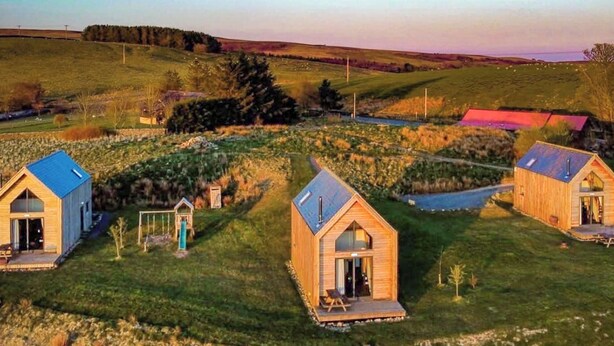 Une propriété rurale comprenant trois cabanes en bois, un petit abri et un sentier.