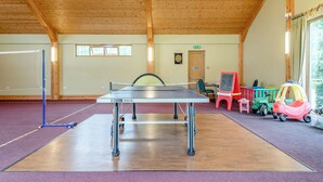 Ein Tischtennistisch in einem Raum mit Holzbalken, einer Dartscheibe und Kinderspielzeug.