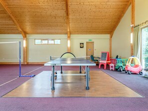 Ein Tischtennistisch in einem Raum mit Holzbalken, einer Dartscheibe und Kinderspielzeug.