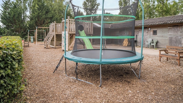 A playground with a trampoline, wooden play structures, and a wooden building in the background. - 2 bedroom accommodation in Blandford Forum (Blandford Forum)