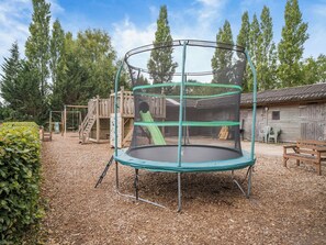 A playground with a trampoline, wooden play structures, and a wooden building in the background.