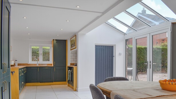 A modern kitchen with dark cabinets, a wooden dining table, and a large window overlooking a garden. - 3 bedroom accommodation in Eakring (Eakring)