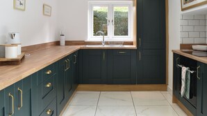 A modern kitchen with dark cabinetry, a wooden countertop, and a window providing natural light. - 3 bedroom accommodation in Eakring (Eakring)