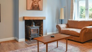 A living room with a stone fireplace, a sofa, a coffee table, and a painting of a bull. - 3 bedroom accommodation in Eakring (Eakring)