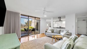 Un salon moderne comprenant un canapé, une petite table, un ventilateur de plafond et une porte-fenêtre coulissante donnant sur un espace extérieur.