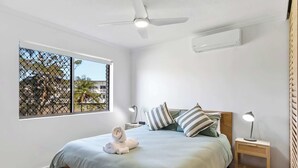 Une chambre à coucher comprenant un lit, une table de chevet, un ventilateur de plafond, une fenêtre et une vue sur l’extérieur.