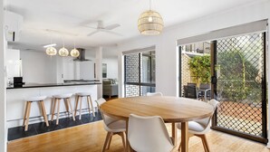Une cuisine moderne avec un coin repas, des meubles blancs et une grande fenêtre donnant sur l’extérieur.