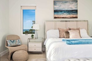 Een slaapkamer met een bed, nachtkastje, stoel, raam met uitzicht en een schilderij aan de muur.