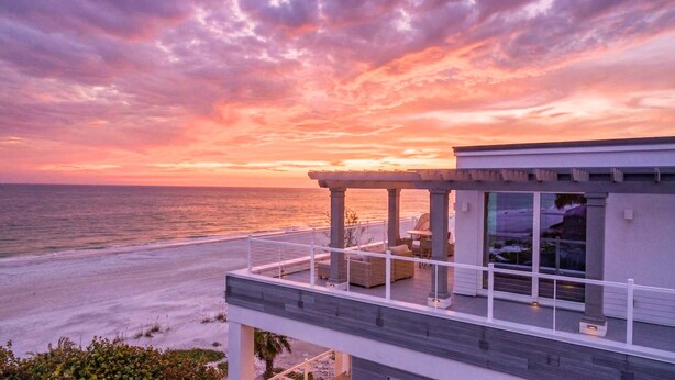 A modern building with a balcony overlooking the ocean at sunset. - Beachfront + Pool/Spa + Elevator + PingPong Table (Indian Rocks Beach)