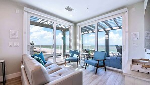 A modern living room with a sofa, chairs, and a view of the beach. - Beachfront + Pool/Spa + Elevator + PingPong Table (Indian Rocks Beach)