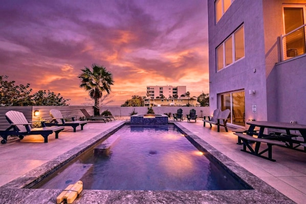 A rooftop pool with lounge chairs, a fire feature, and a view of a building with multiple floors.