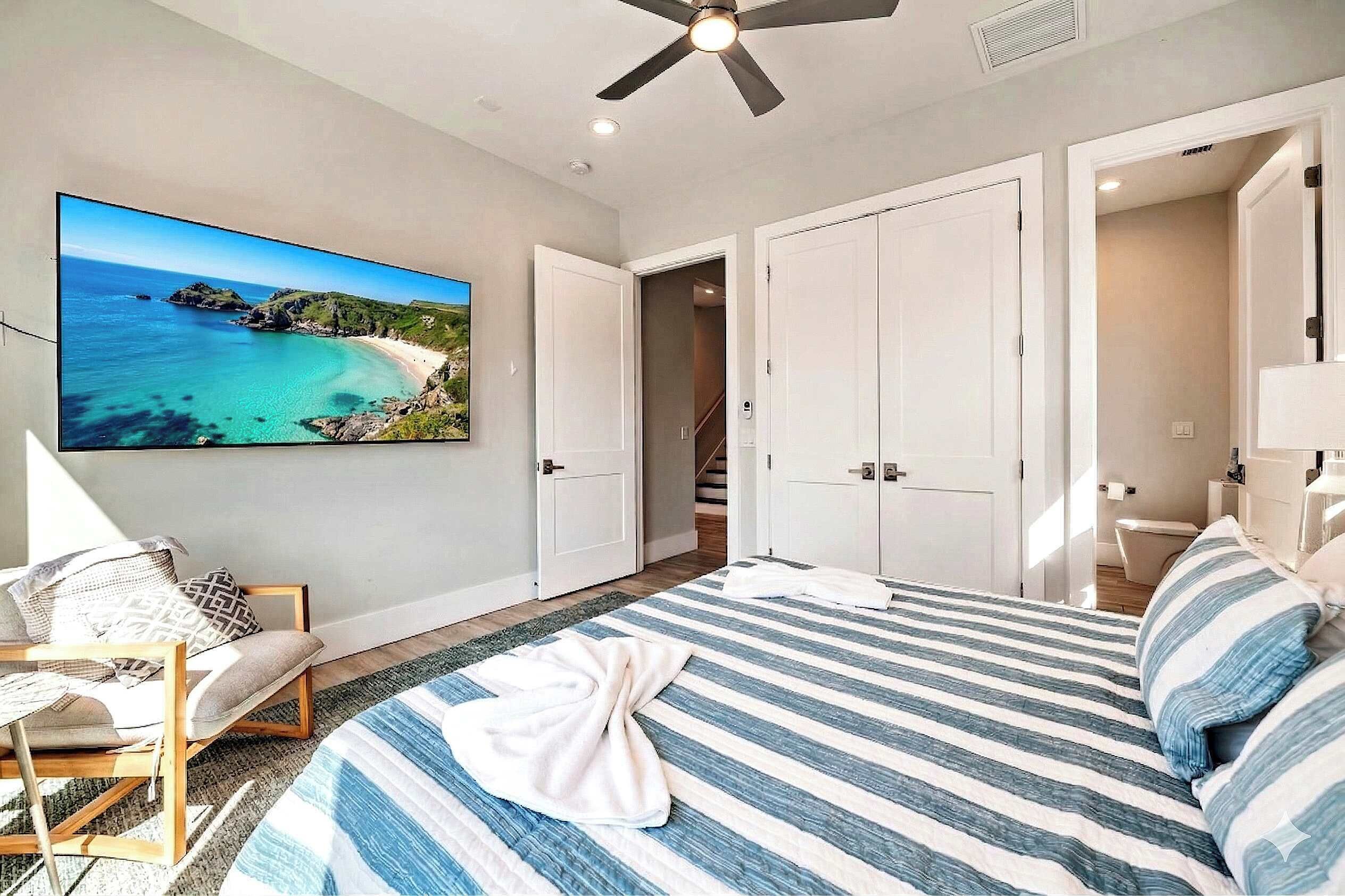 A bedroom with a bed, a chair, a ceiling fan, and a large window.