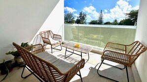 Ein Balkon mit Korbmöbeln, einem Tisch und einem Blumentopf.