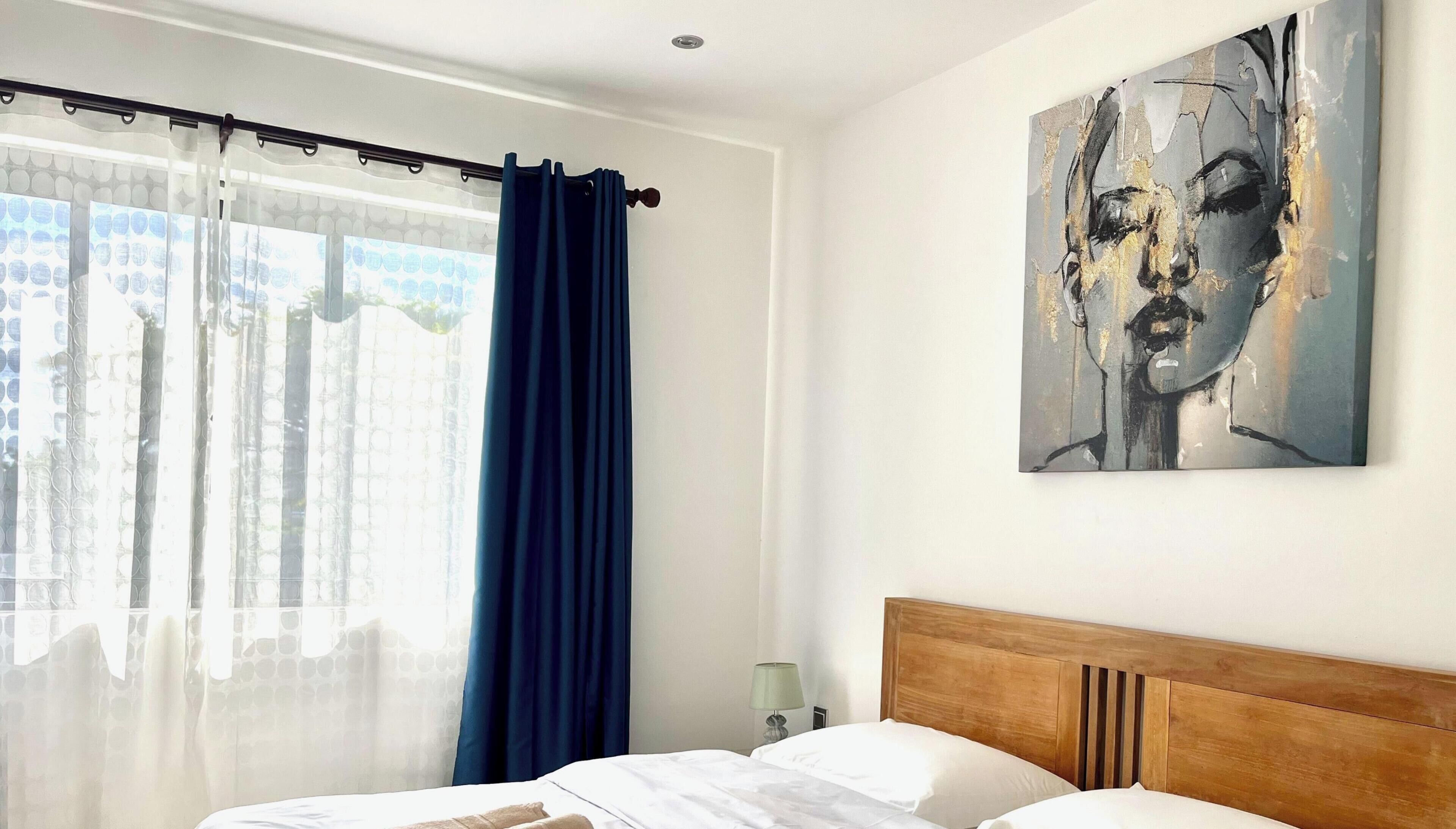 Habitación de hotel con cama, cabecero, un cuadro y una ventana con cortinas.
