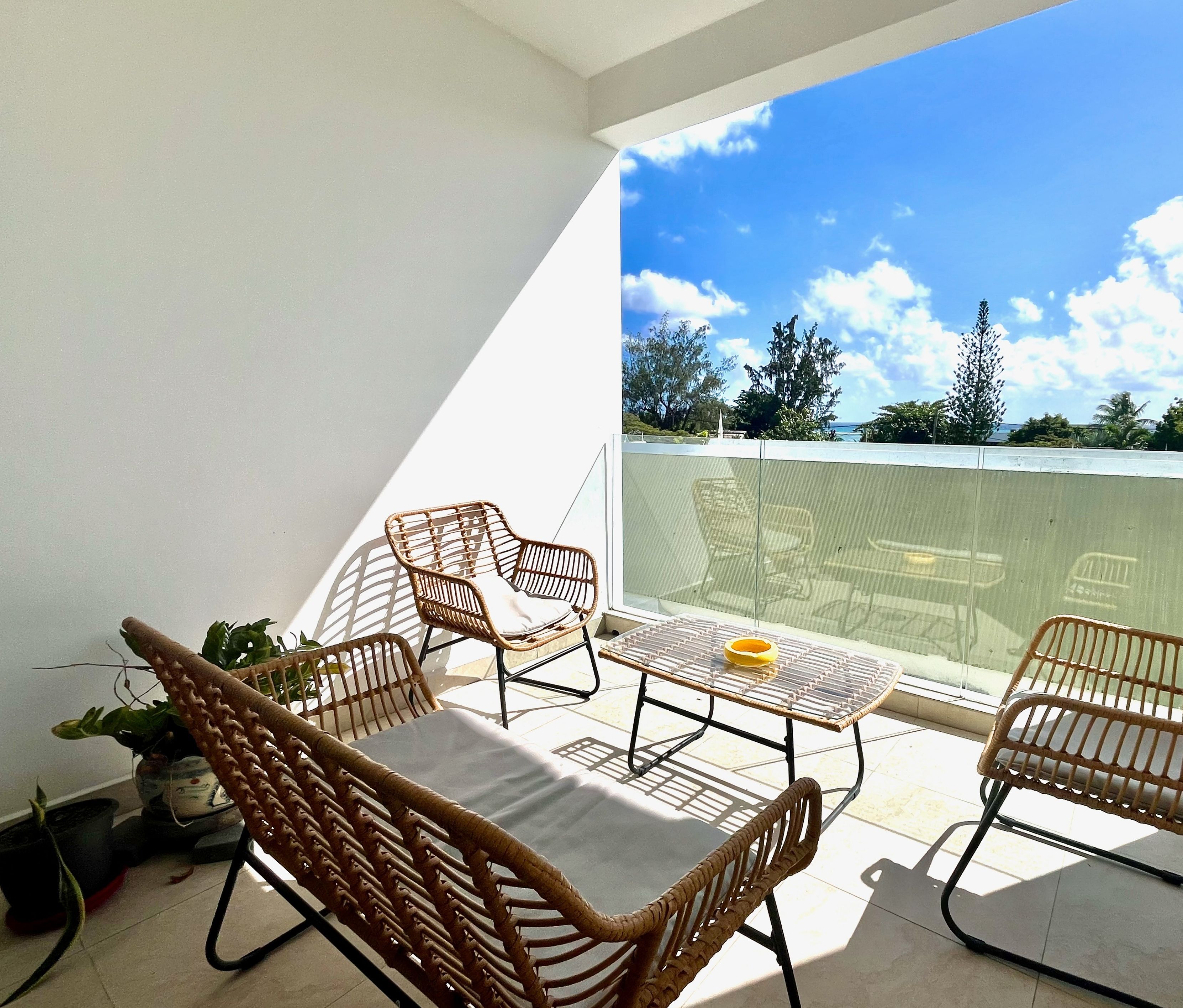 A balcony with wicker furniture, a table, and a potted plant.