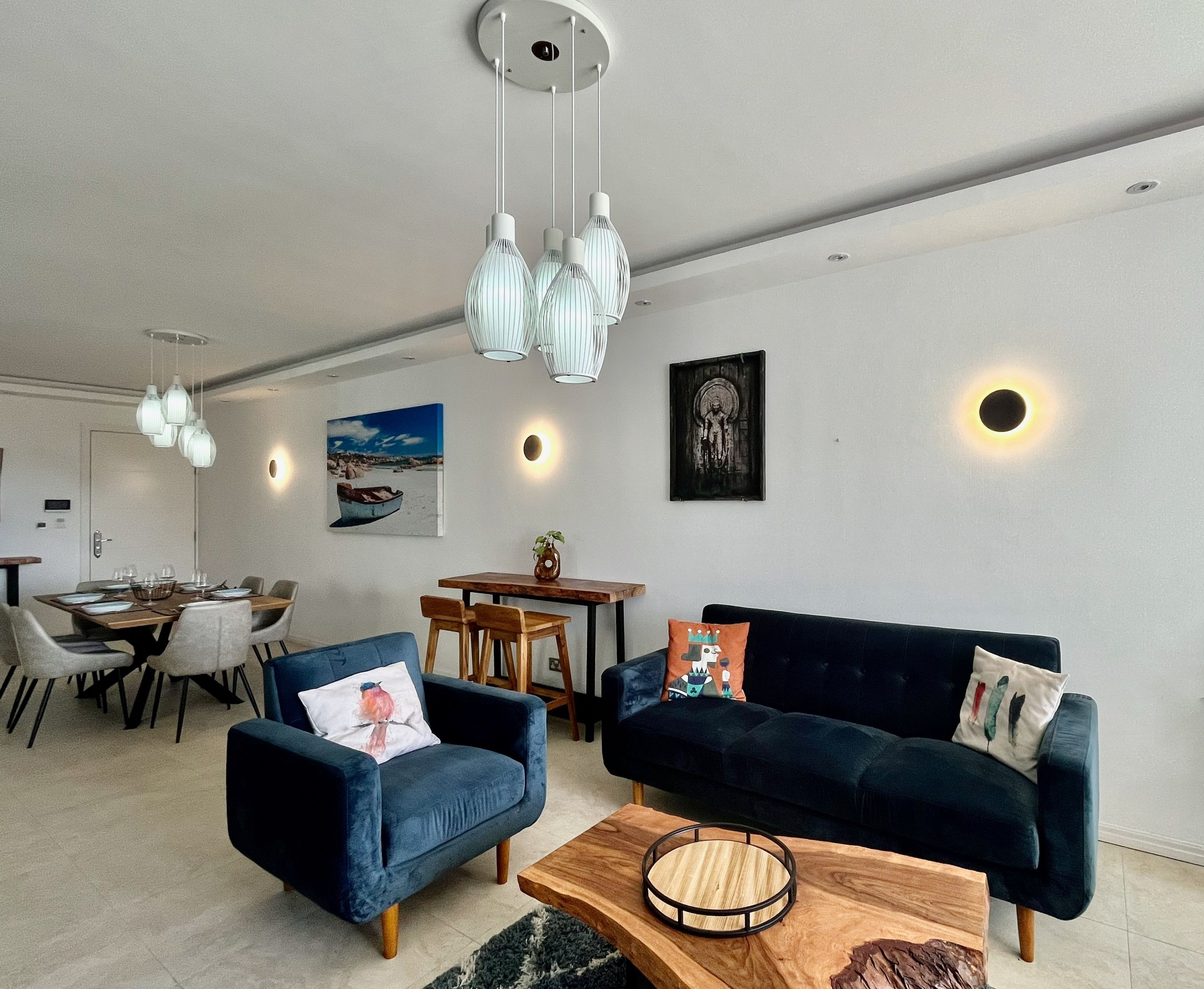 A modern living room with a dark blue sofa, a wooden coffee table, and a dining area with a wooden table and chairs.