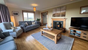A living room with a sofa, a coffee table, a fireplace, and a television. - Airigh nam Fiadh (South Uist)