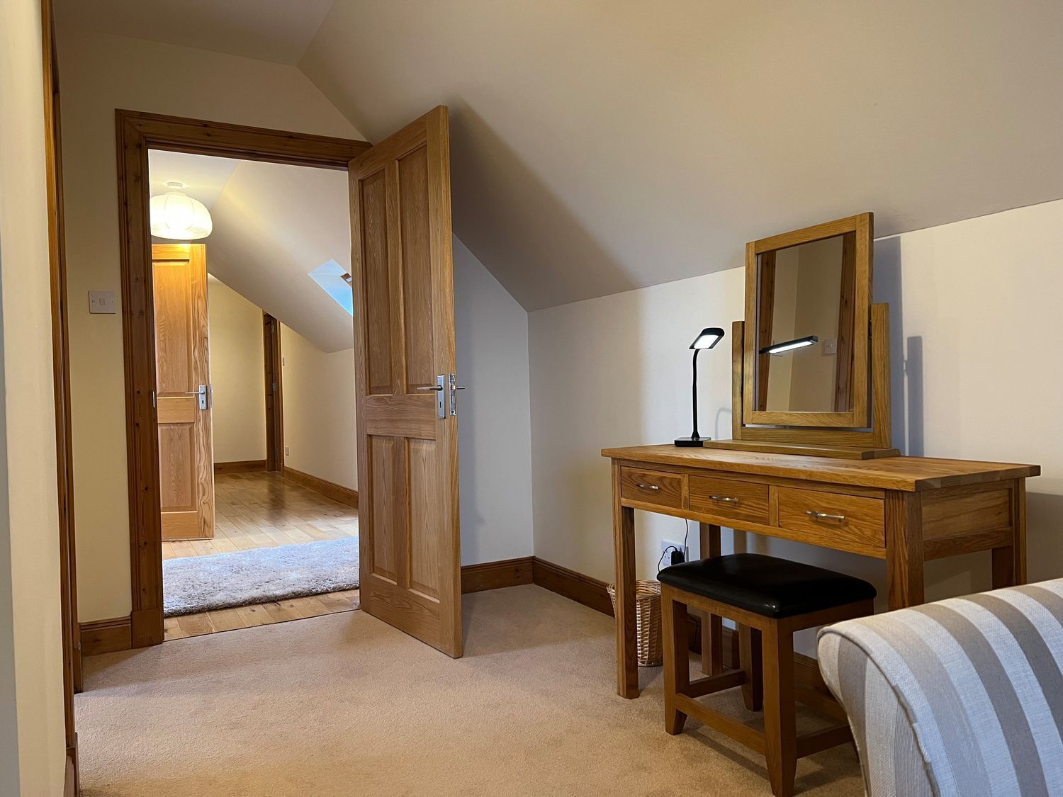Een slaapkamer met een houten bureau, een spiegel, een bedlamp en een raam met uitzicht op een gang.