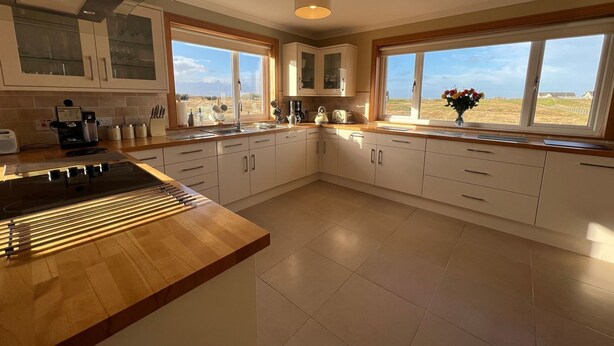 A modern kitchen with white cabinets, a wooden countertop, and large windows offering a view of the countryside. - Airigh nam Fiadh (South Uist)