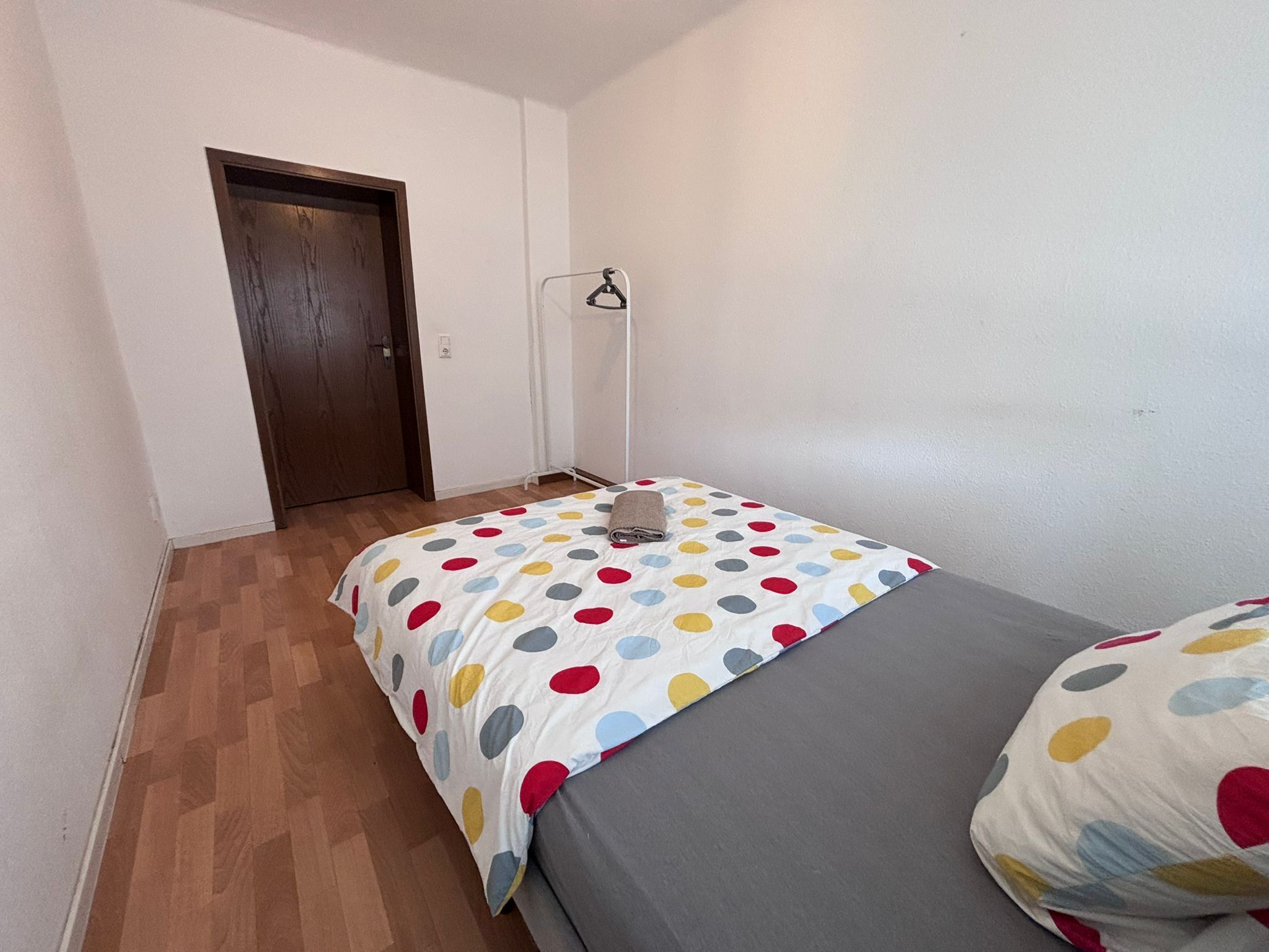 A small, single-bed room with a wooden floor, a white door, and a bed with a polka dot bedspread.