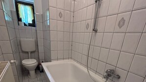 A bathroom with a white bathtub, a toilet, and tiled walls. - Spacious Central 3Bedroom flat for 8 guests (Zeitz)