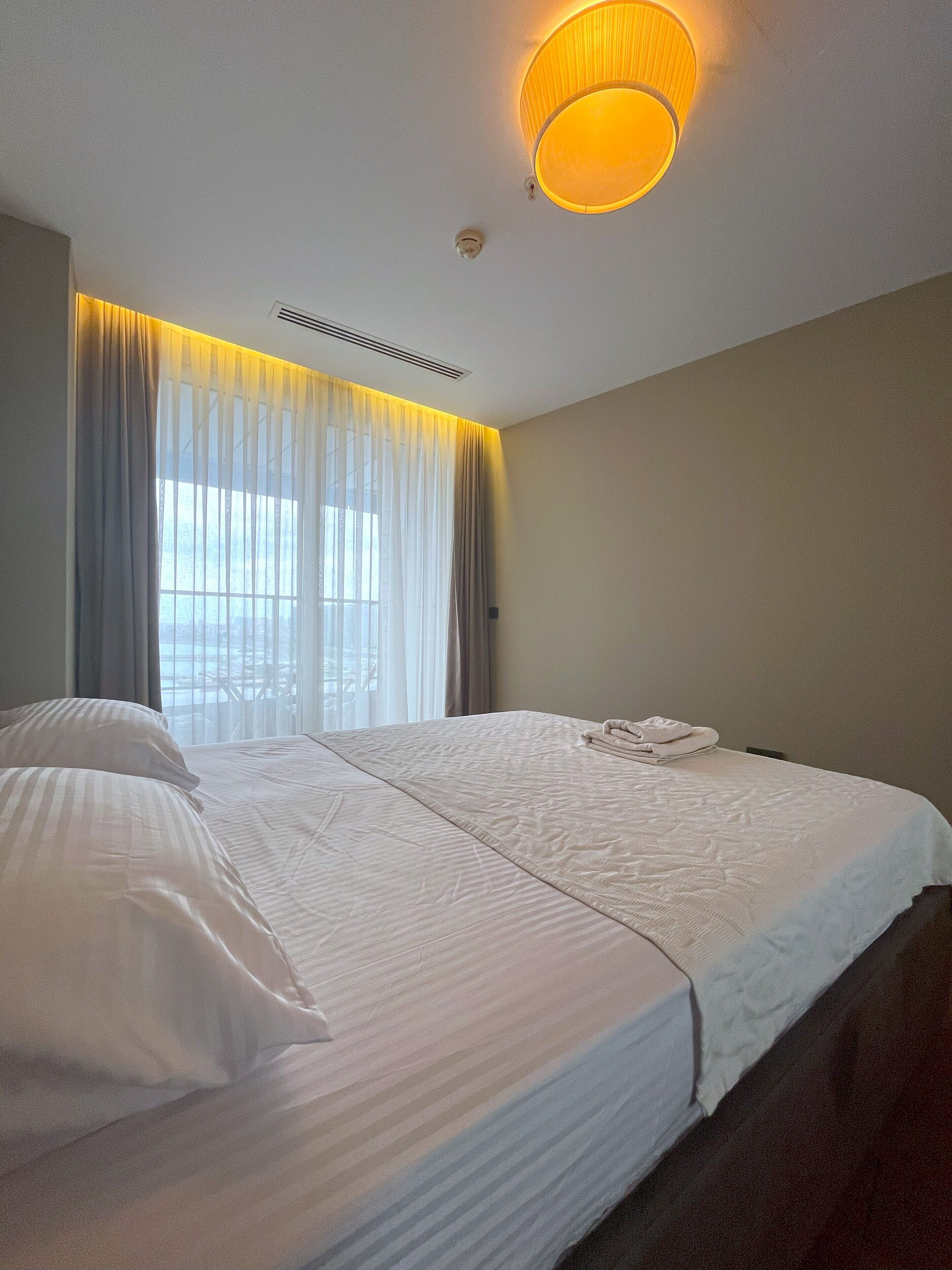 A hotel room with a large bed, a ceiling light, and a window with curtains.