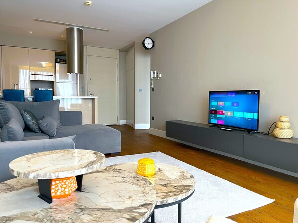 A modern living room with a sofa, a coffee table, a flat-screen TV, and a kitchen area in the background. - Flex Ottomare Suites (İstanbul)