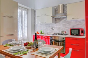 A modern kitchen with red cabinets, a microwave, a stove, and a dining area set with plates, glasses, and a bottle. - Il Nido Di Ale (Sanremo)
