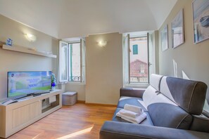 Una sala de estar moderna con un televisor de pantalla plana, un sofá, una mesita y un ventanal con vista a un edificio.