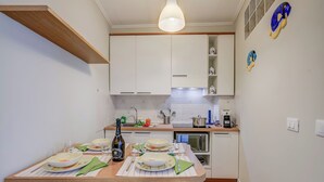 Uma cozinha moderna com armários brancos, bancada de madeira e área de refeições preparada para quatro pessoas.