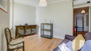 A living room with a wooden floor, a sofa, a chair, a glass shelving unit, and a hanging light fixture. - Armonia Centrale - Sanremo Apt for 4 With A/C (Sanremo)