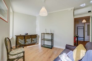 A living room with a wooden floor, a sofa, a chair, a glass shelving unit, and a hanging light fixture. - Armonia Centrale - Sanremo Apt for 4 With A/C (Sanremo)