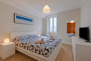 A modern bedroom with a bed, bedside tables, a desk, a television, and a window. - Armonia Centrale - Sanremo Apt for 4 With A/C (Sanremo)
