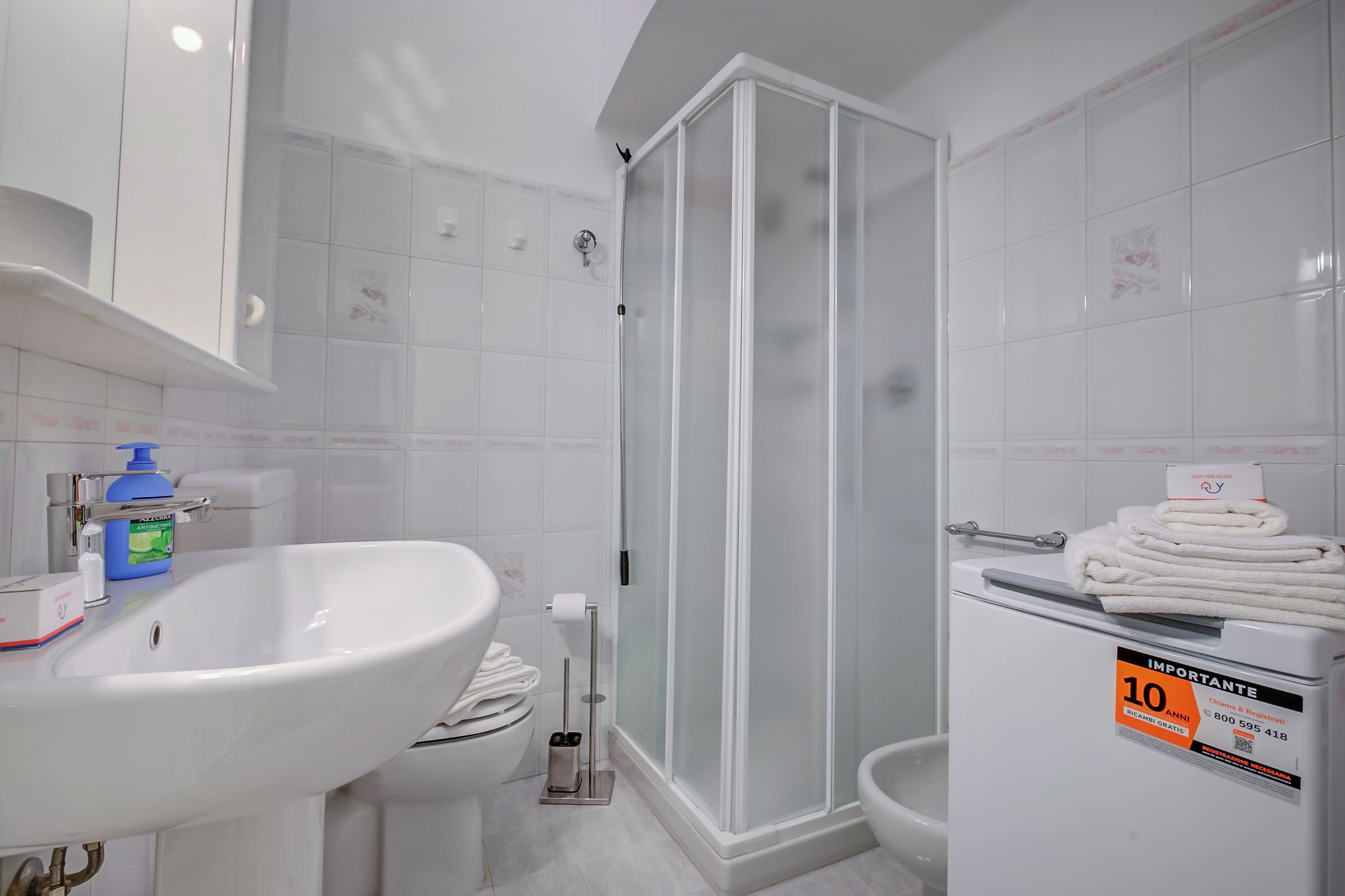 Une salle de bain avec un lavabo blanc, une cabine de douche en verre et un porte-serviettes avec des serviettes pliées.