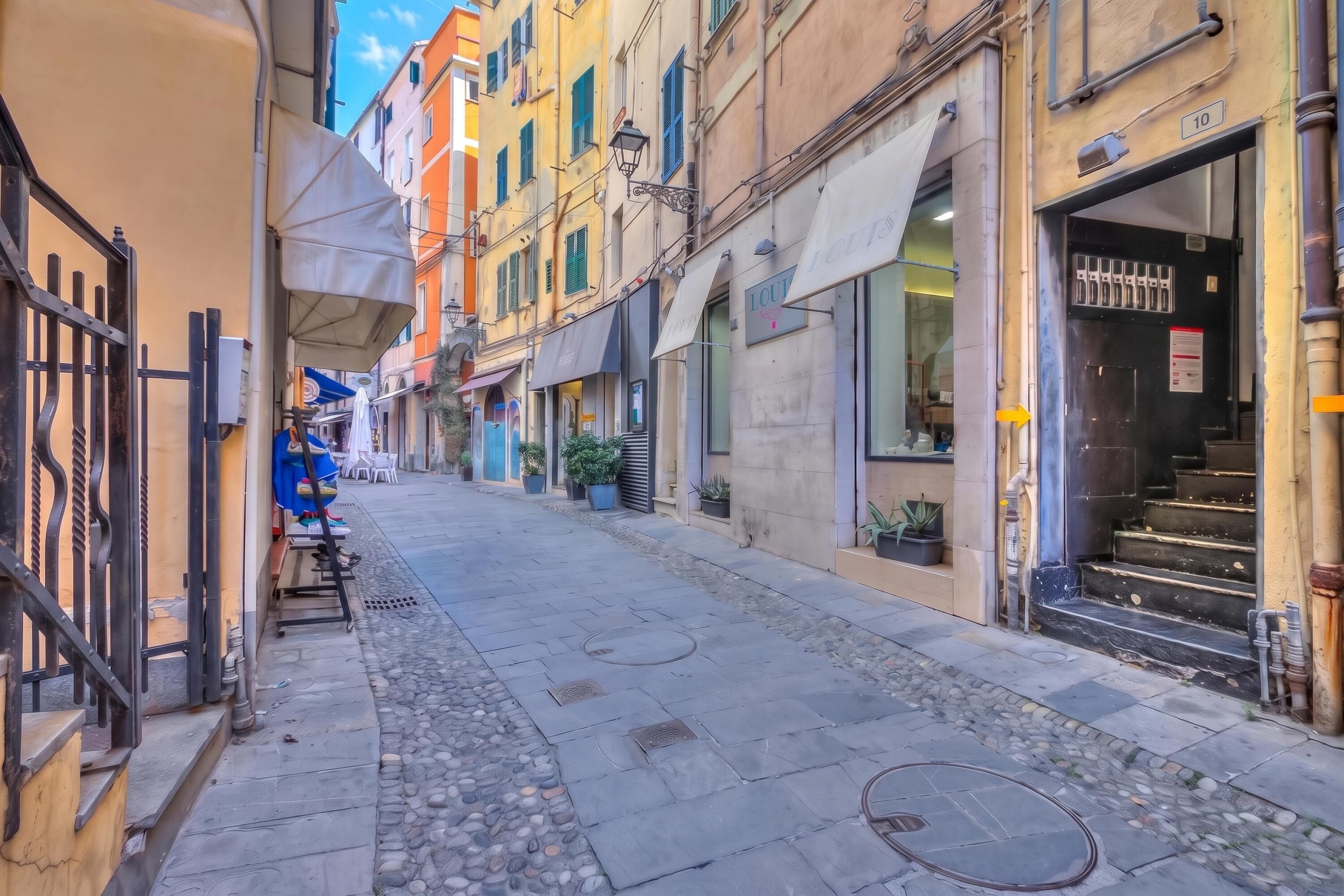 A narrow street with buildings on either side, a gate on the left, and a storefront with a sign on the right.