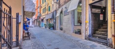 A narrow street with buildings on either side, a gate on the left, and a storefront with a sign on the right.