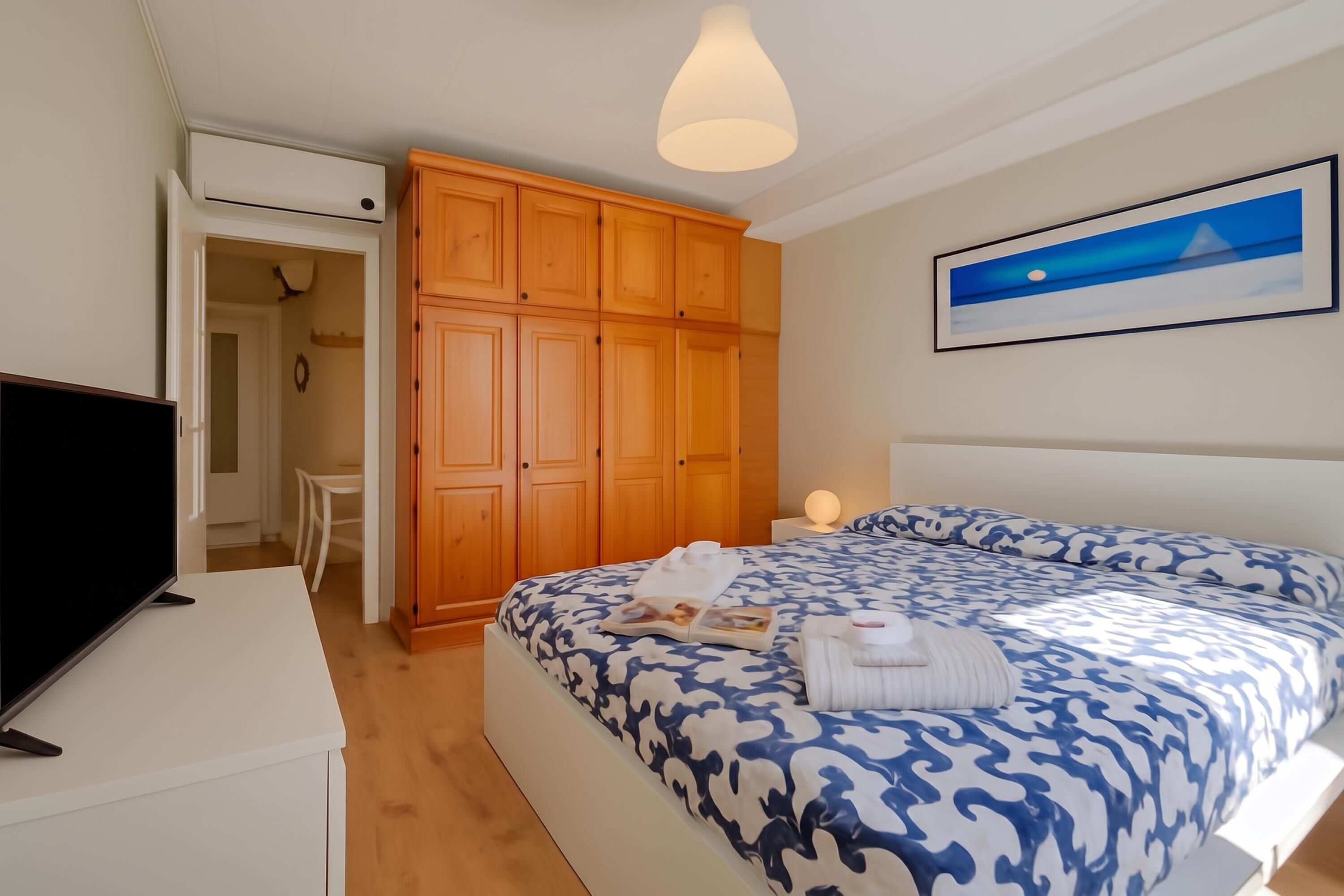 A bedroom with a bed, a television, wooden wardrobe, and a painting on the wall.