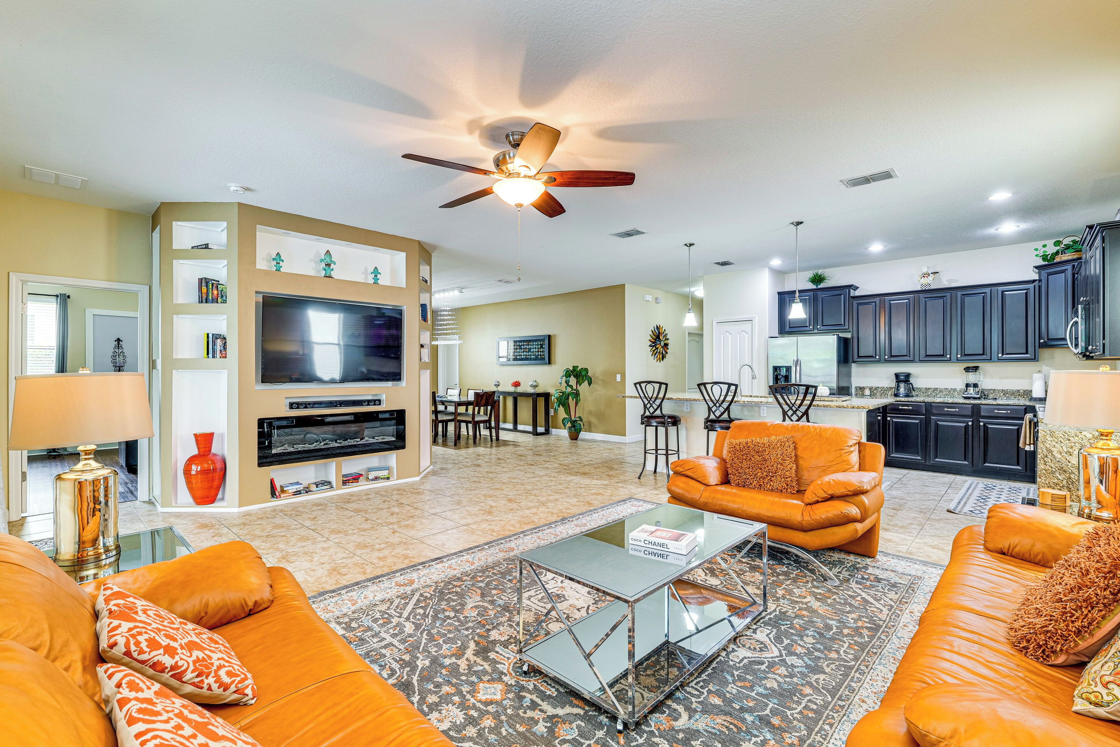 A modern living room with a flat-screen TV, leather sofas, a coffee table, and a ceiling fan.