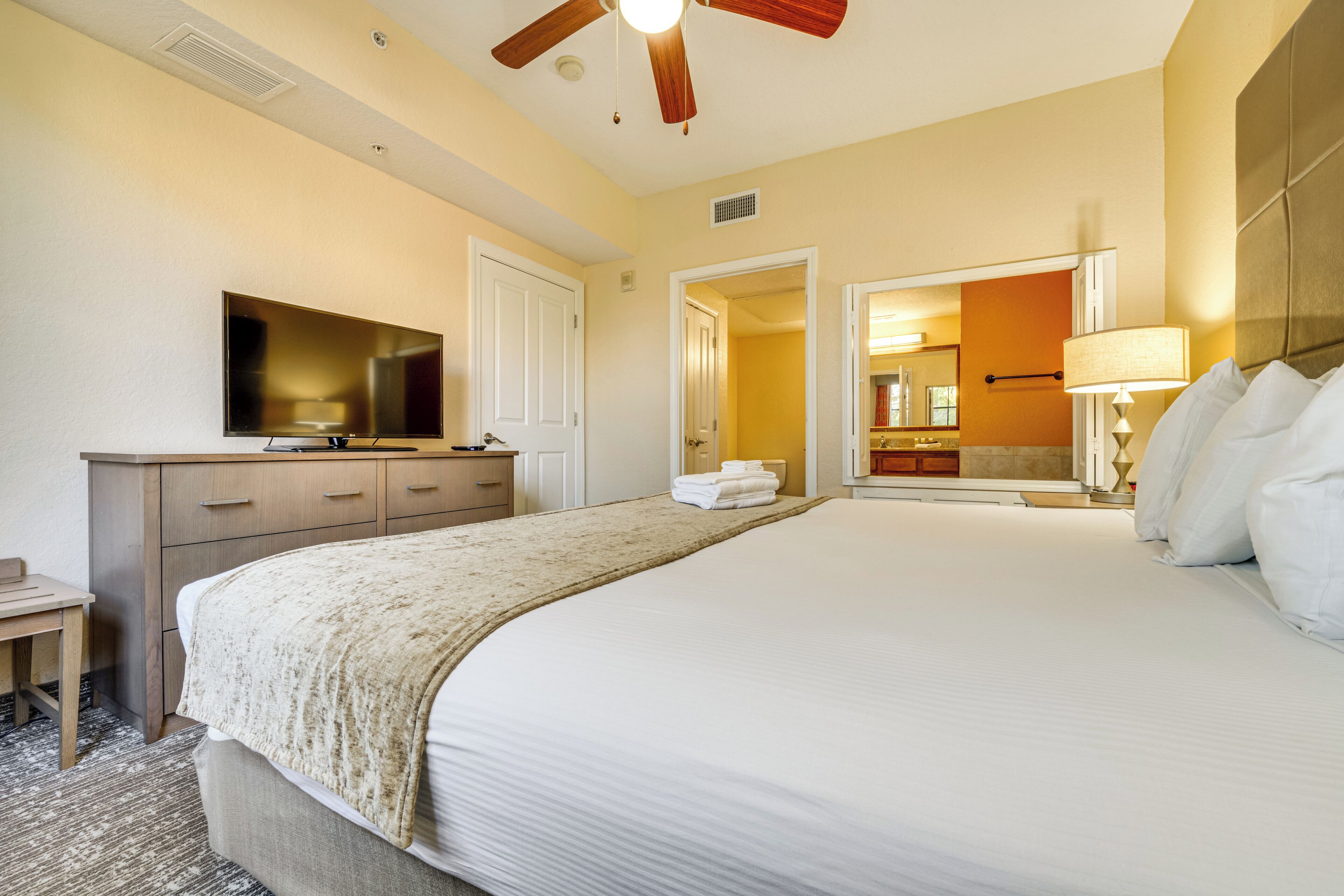 A hotel room with a large bed, a TV, a desk, and a ceiling fan.
