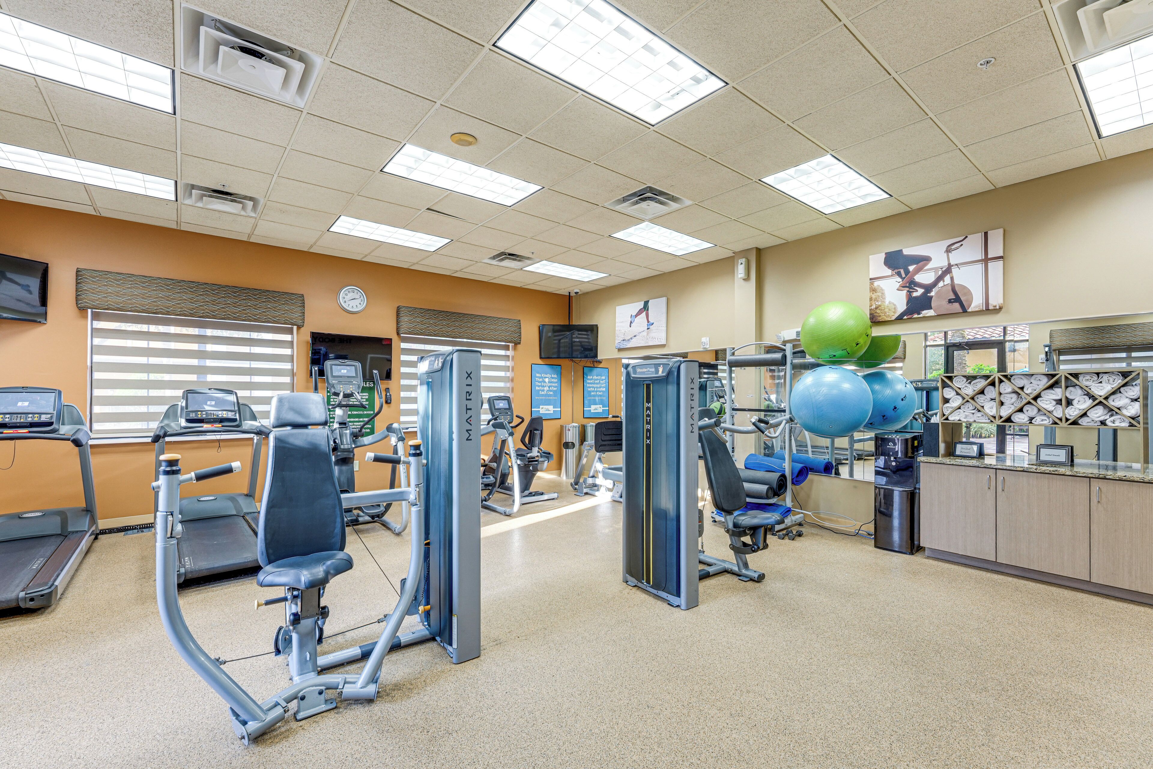 Un gimnasio con diversos equipos de ejercicio, un mostrador de recepción y un reloj de pared.
